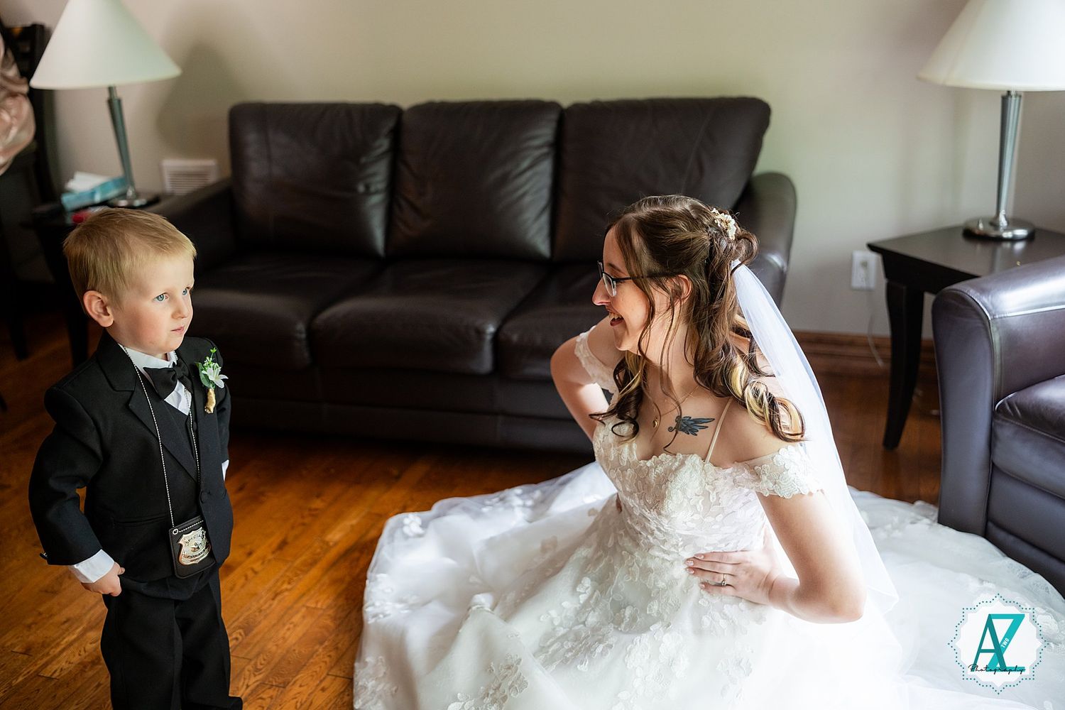 A touching wedding moment between a bride in a white dress and young ring bearer in a suit standing in a living room.