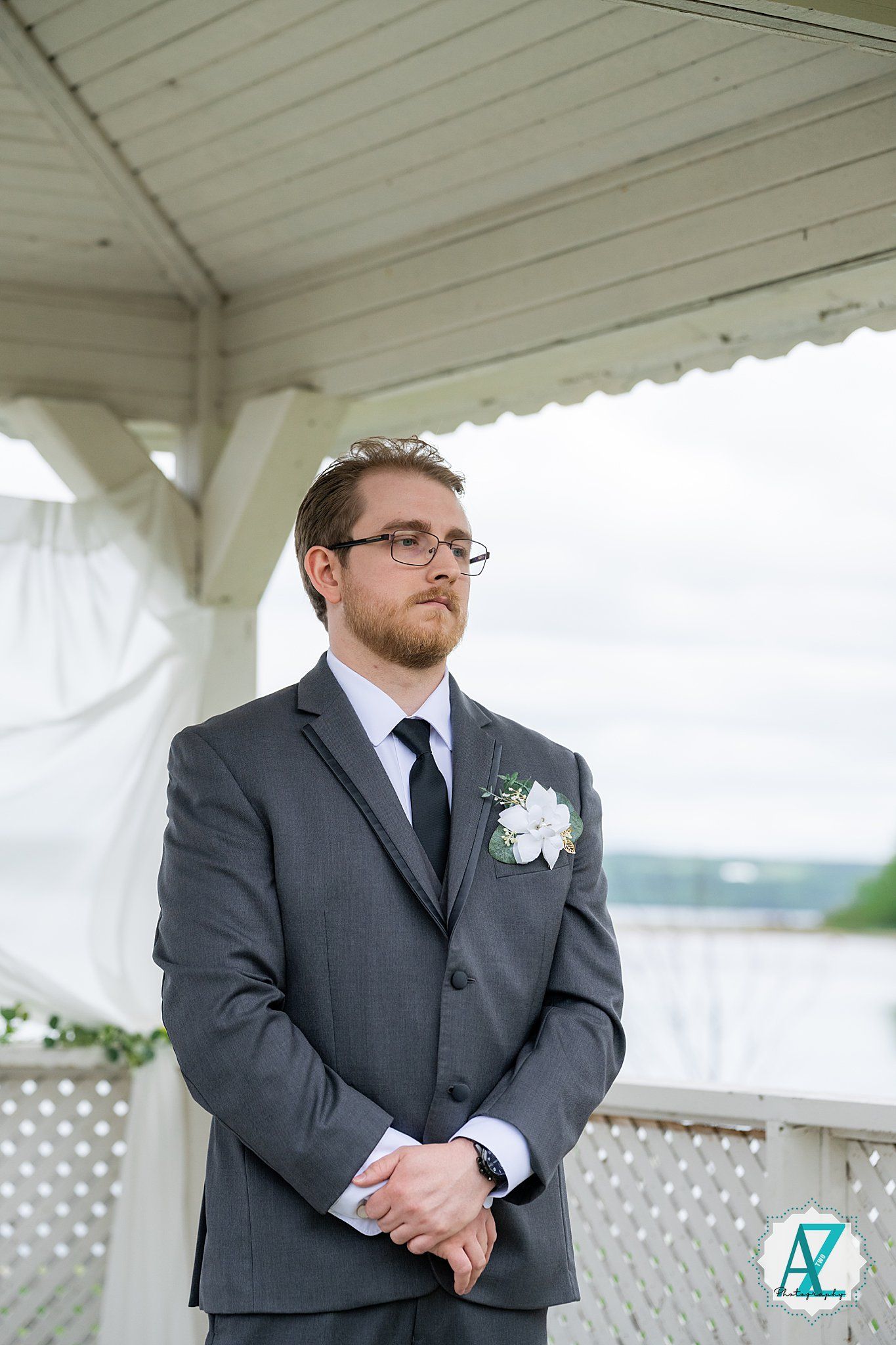 A man in a dark suit and tie stands in front of a white latticed gazebo during a formal event.