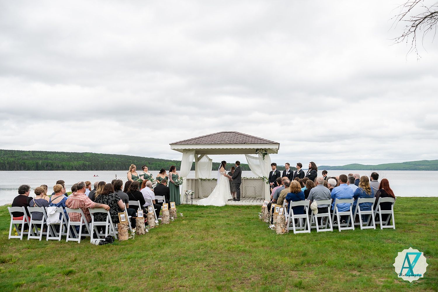 Wedding ceremony setup with white chairs and a waterfront gazebo overlooking a lake under cloudy skies.