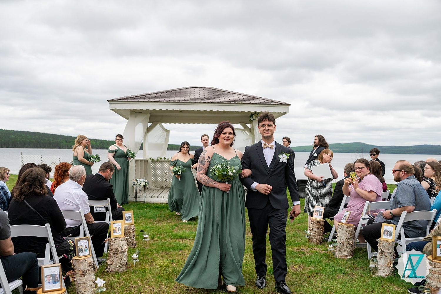 Wedding party celebrates outdoors against a scenic coastal backdrop with cloudy skies and mountains in the distance.
