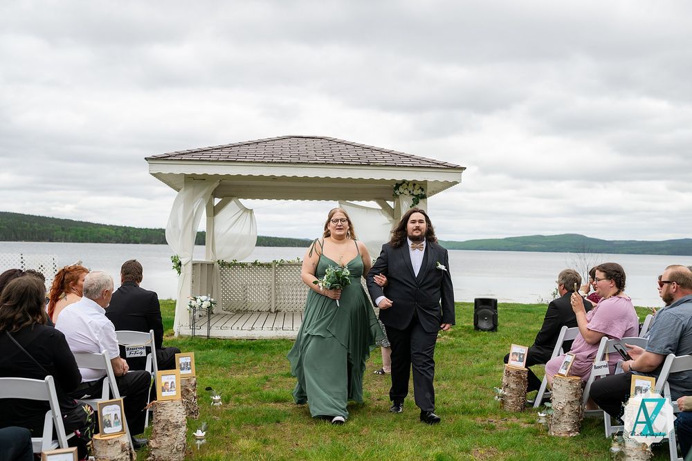 Wedding ceremony on grassy lawn with white gazebo overlooking a serene lake under cloudy skies.