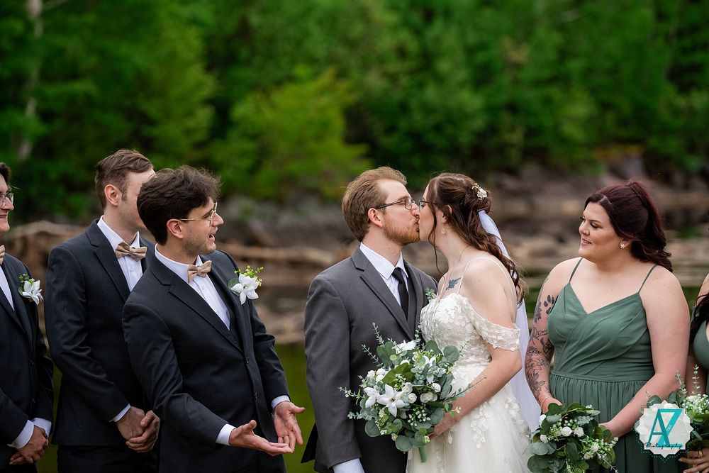 Members of a wedding party gather outdoors against a lush green forest backdrop during a romantic ceremony.