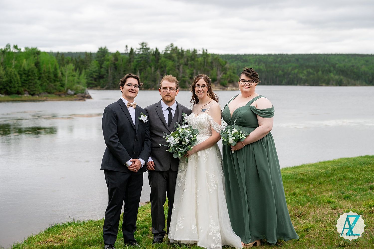 Wedding party poses together on a rainy day by a scenic lake with trees and cloudy skies in the background.