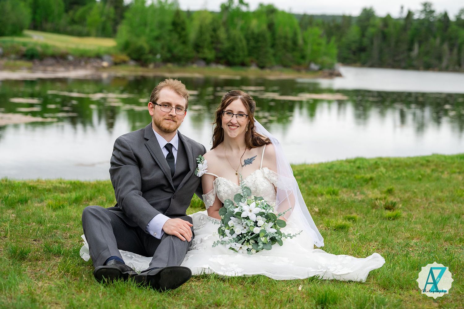 Bride and groom pose together in white dress and black suit by a serene lakeside setting for wedding photos.
