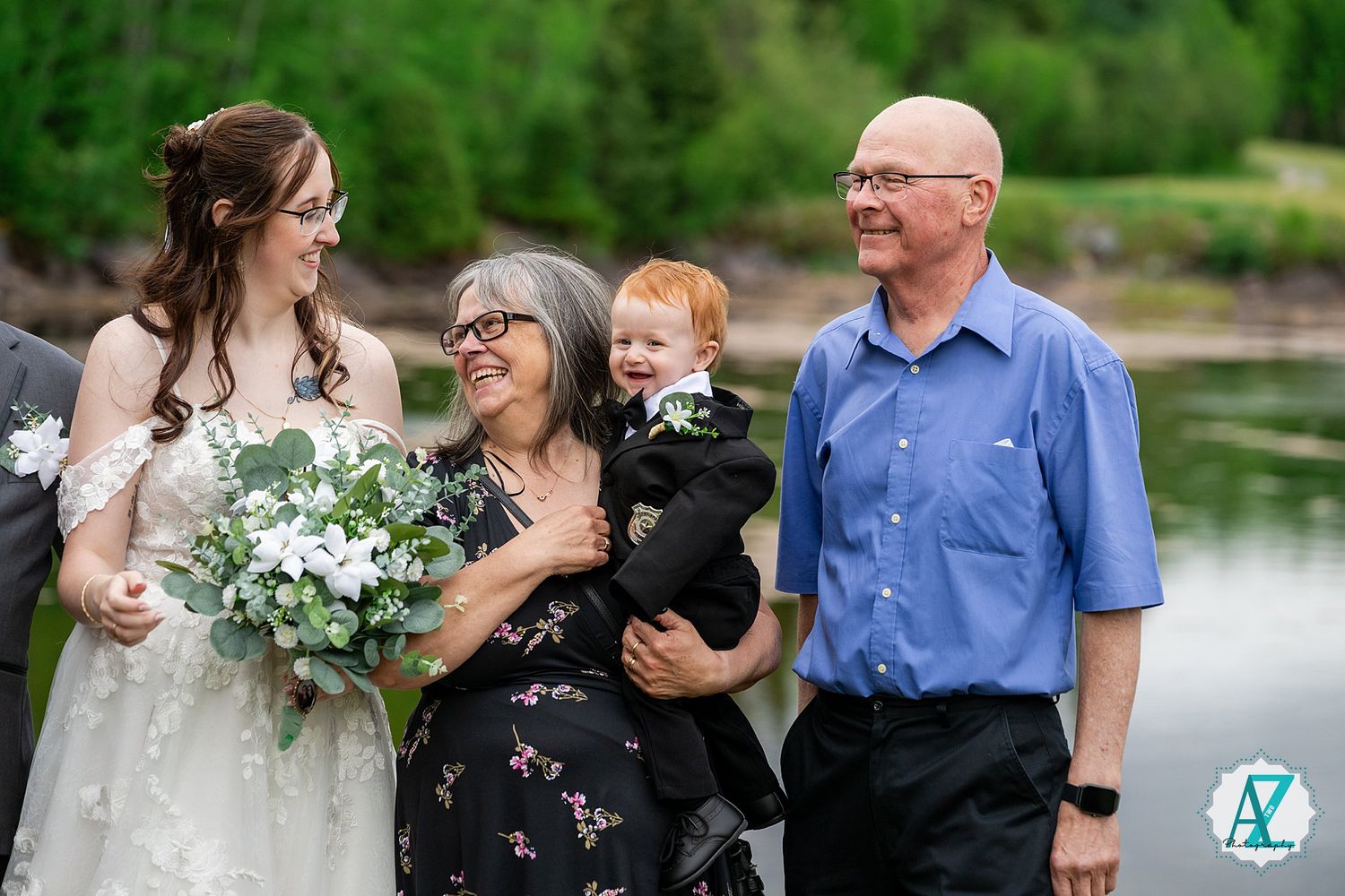 A wedding celebration at a lakeside location with a bride holding a white and green bouquet in summer.
