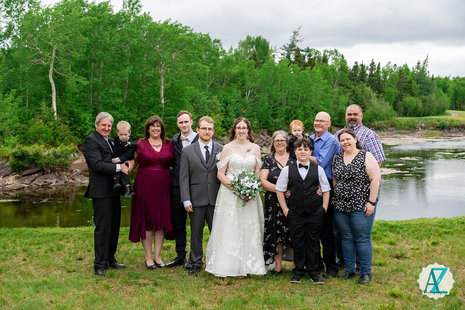 Wedding party poses together beside a river with green trees and natural scenery in the background.