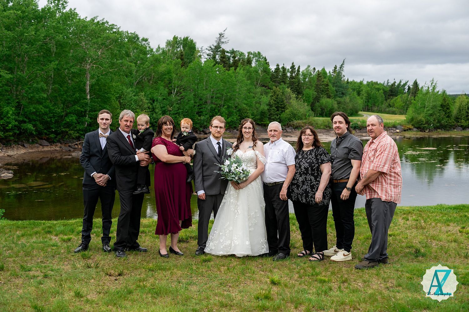 Wedding party members stand together for outdoor group photos by a serene lake on an overcast day.