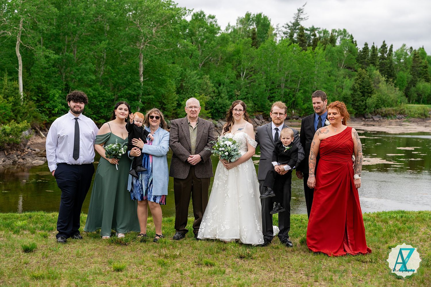 Wedding party poses together in front of a lush green landscape during an outdoor summer celebration.