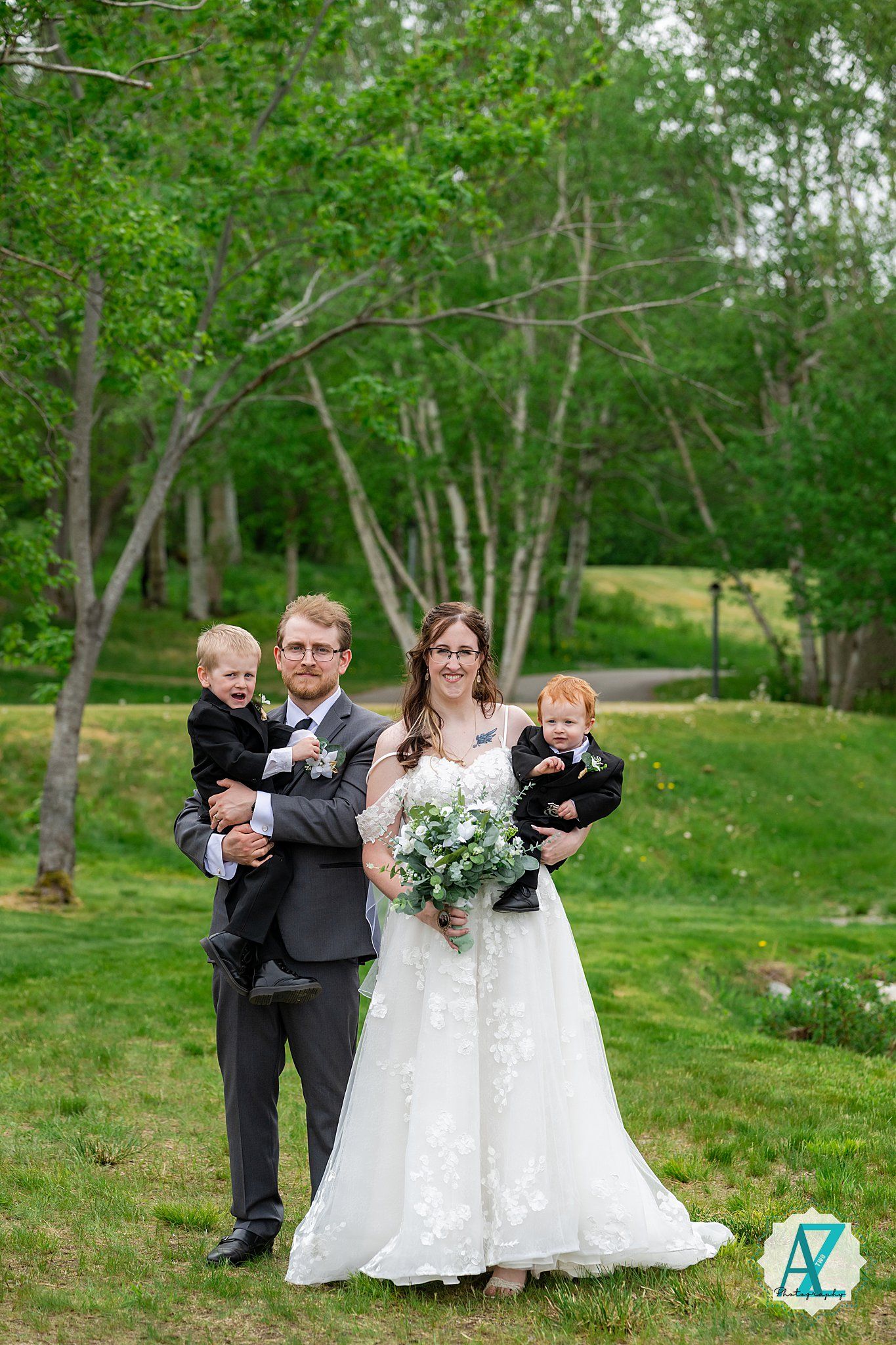 A joyful wedding party poses outdoors in a lush green park setting.