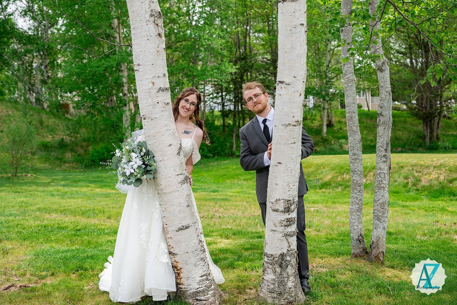 A bride and groom pose between white birch trees with blue and white wildflower bouquet at an outdoor wedding.