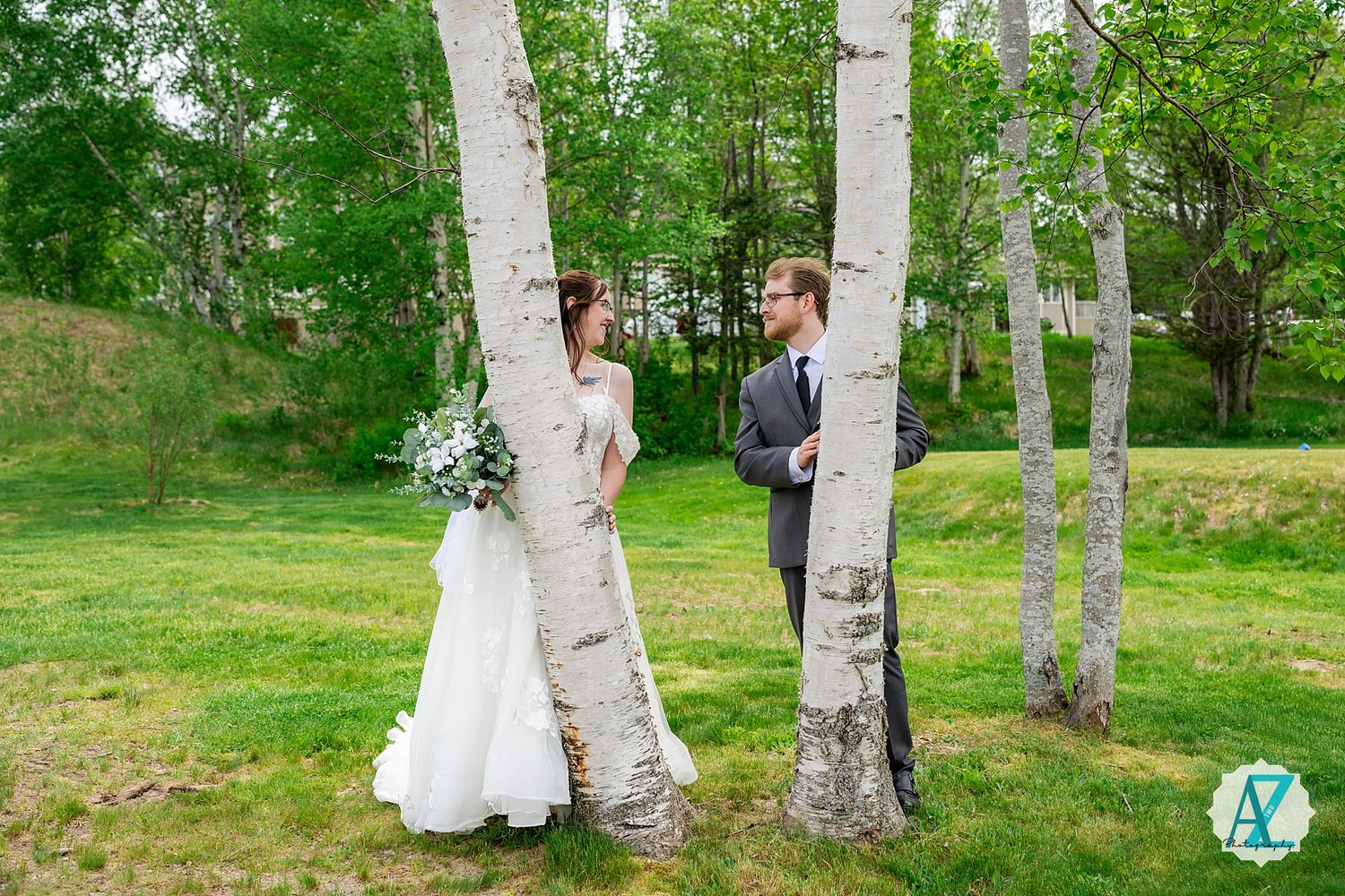 A couple embrace between birch trees in a lush green outdoor setting during their wedding day celebration.
