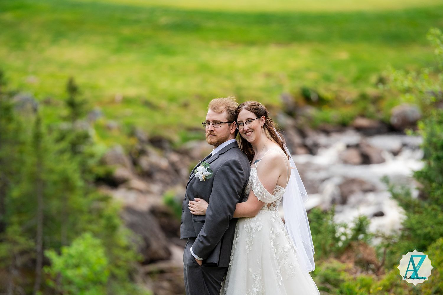 Couple shares intimate moment surrounded by lush green landscape and rushing stream.