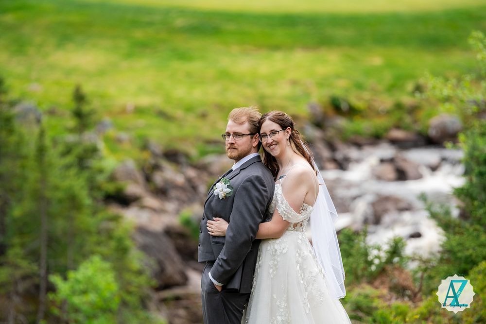 Couple shares intimate moment surrounded by lush green landscape and rushing stream.
