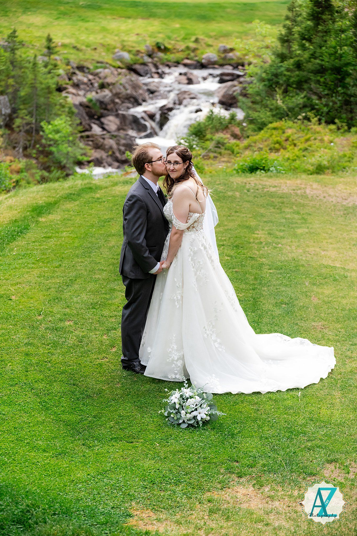 A romantic wedding photo captured against a mountain stream backdrop on a lush green hillside.