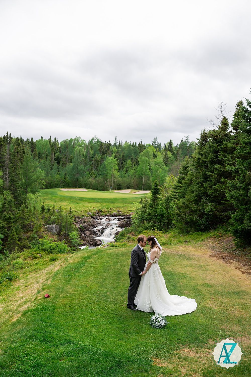 Scenic wedding portrait on a golf course with cascading stream and evergreen forest in the background.