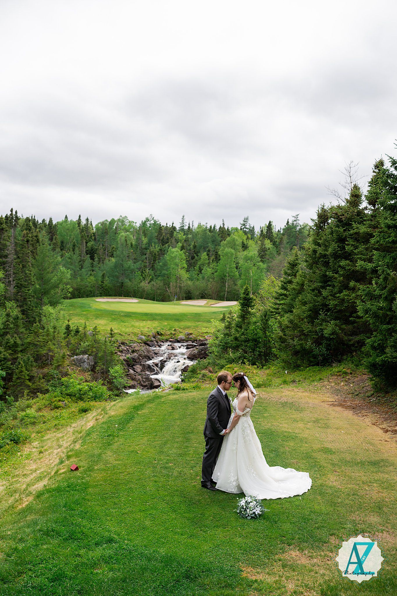 Scenic wedding portrait on a golf course with cascading stream and evergreen forest in the background.
