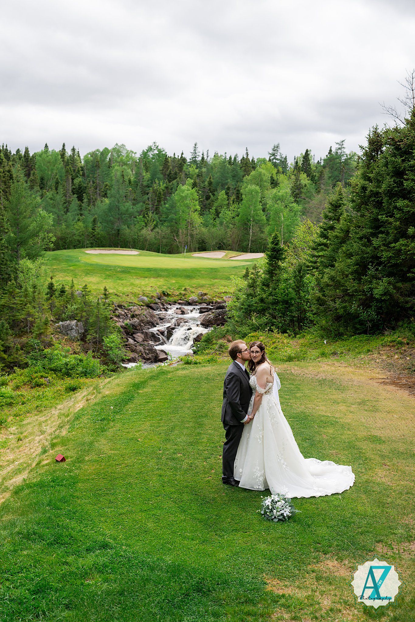 A scenic wedding ceremony takes place on a lush green golf course with a cascading waterfall and evergreen trees in the background.