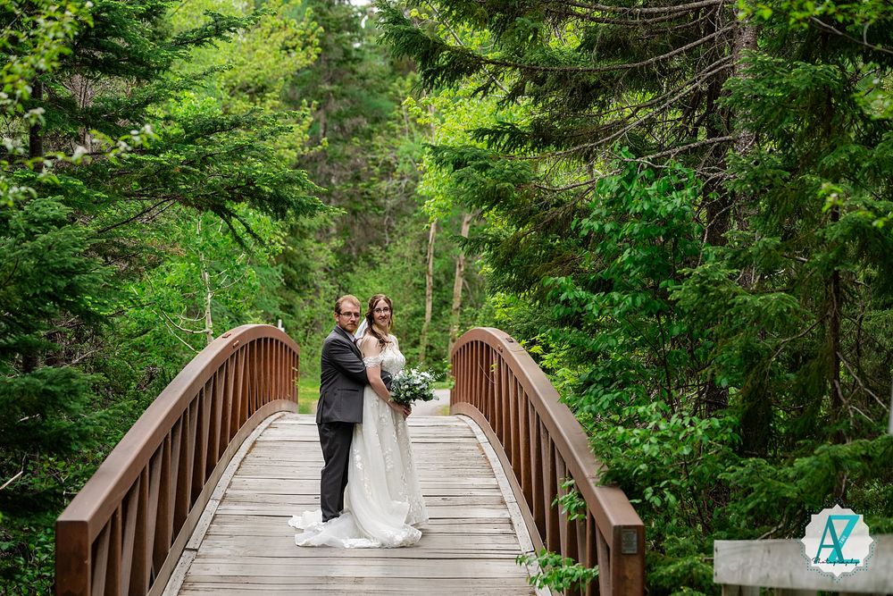 A romantic wedding photo captured on a wooden bridge with towering evergreens in the background.