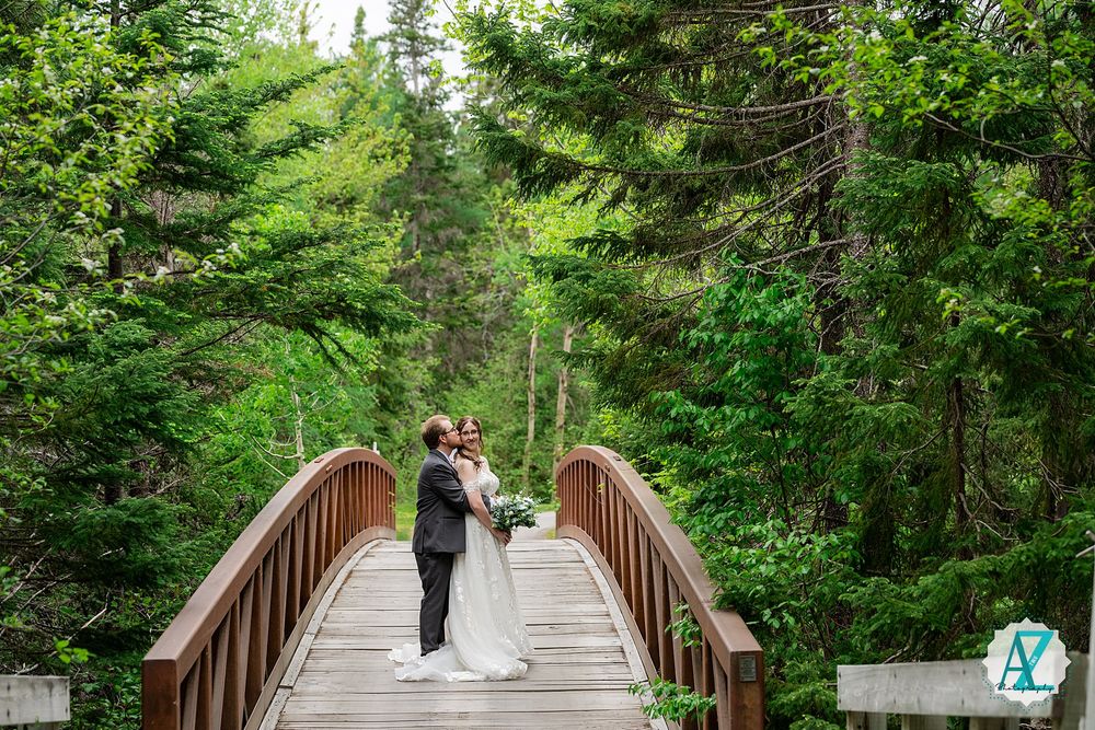 Wooden footbridge crosses through lush green forest with couple standing in peaceful natural setting.