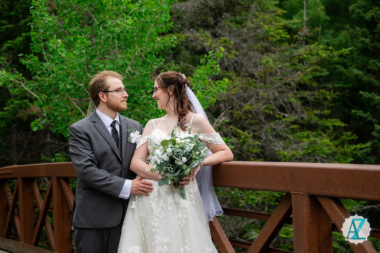 A bride and groom share a romantic moment on a wooden bridge surrounded by lush green foliage.