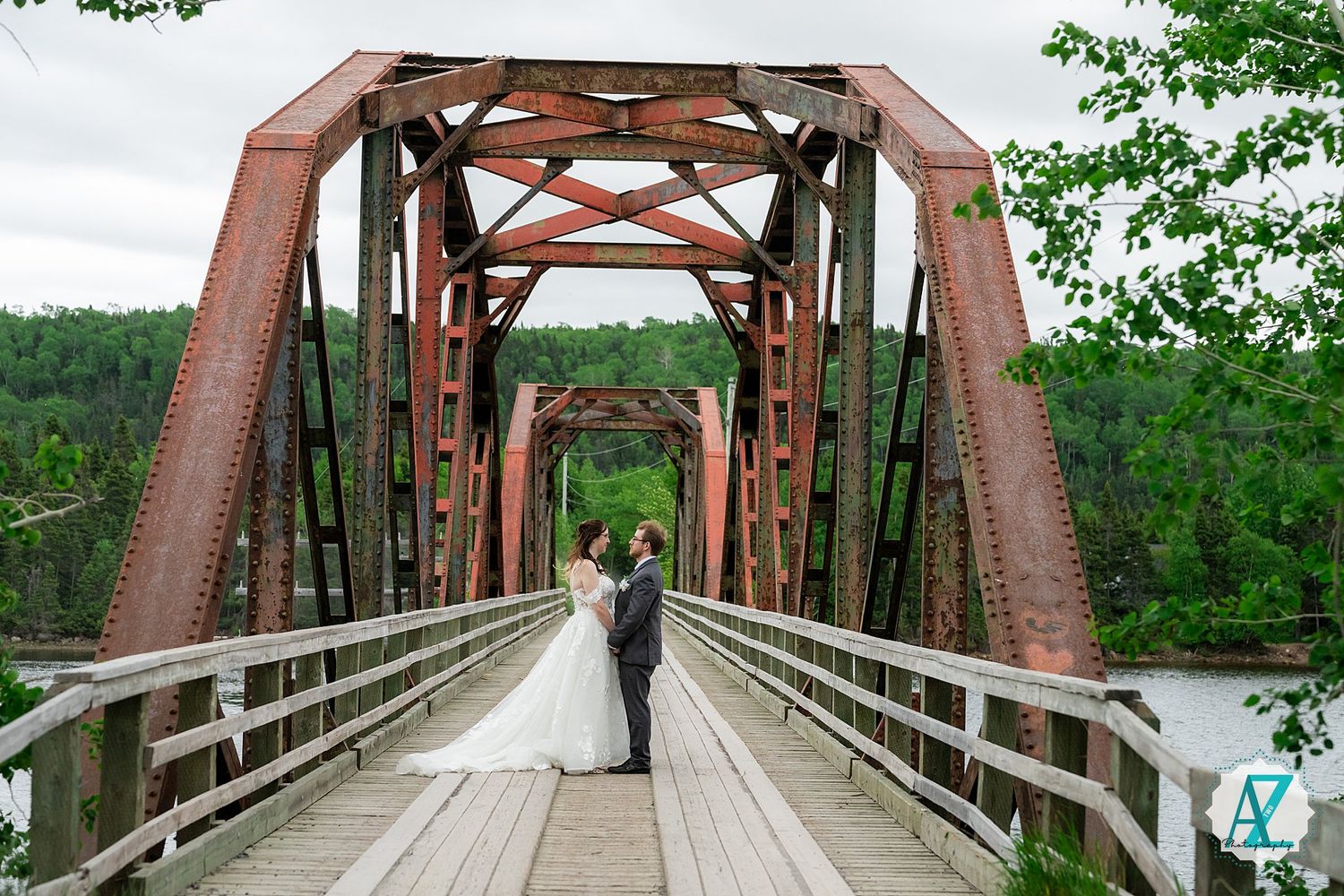 A couple shares a tender moment on a rustic steel and wooden bridge spanning across a scenic river.