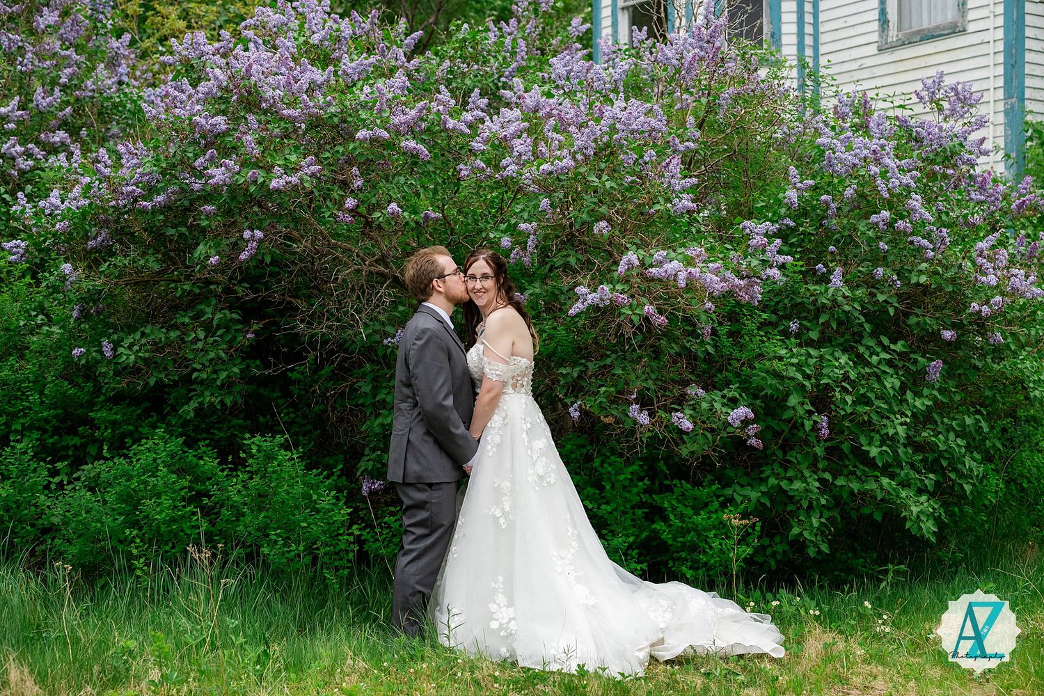 A newlywed couple stands together in front of blooming purple lilac bushes during a springtime garden wedding.