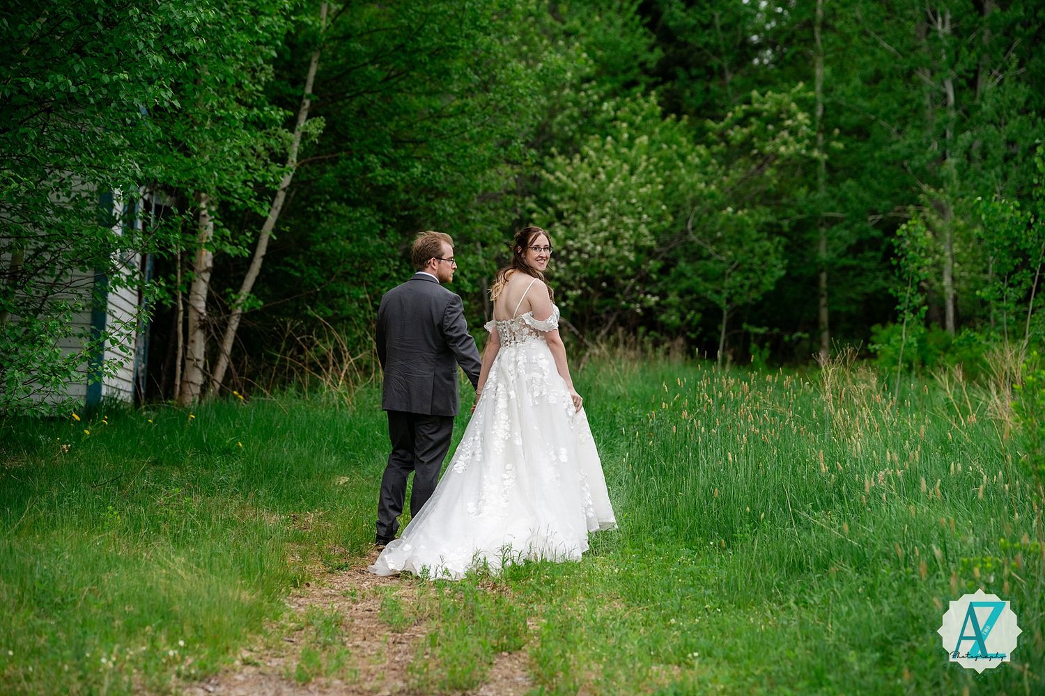 A couple walks through a lush green forest path during their outdoor wedding celebration.