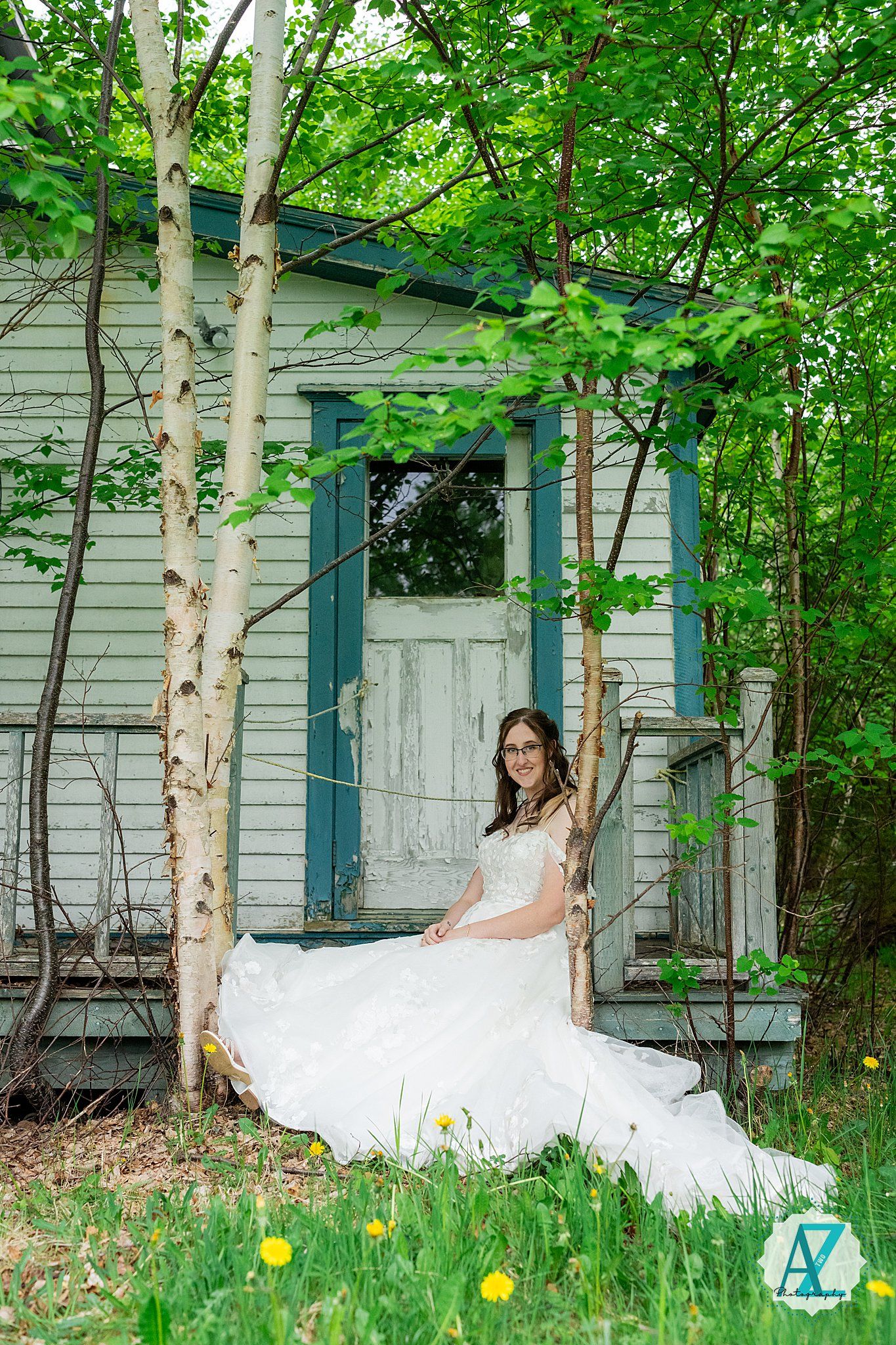 Rustic white wedding dress flowing on a swing by birch trees near a vintage cottage surrounded by spring greenery.