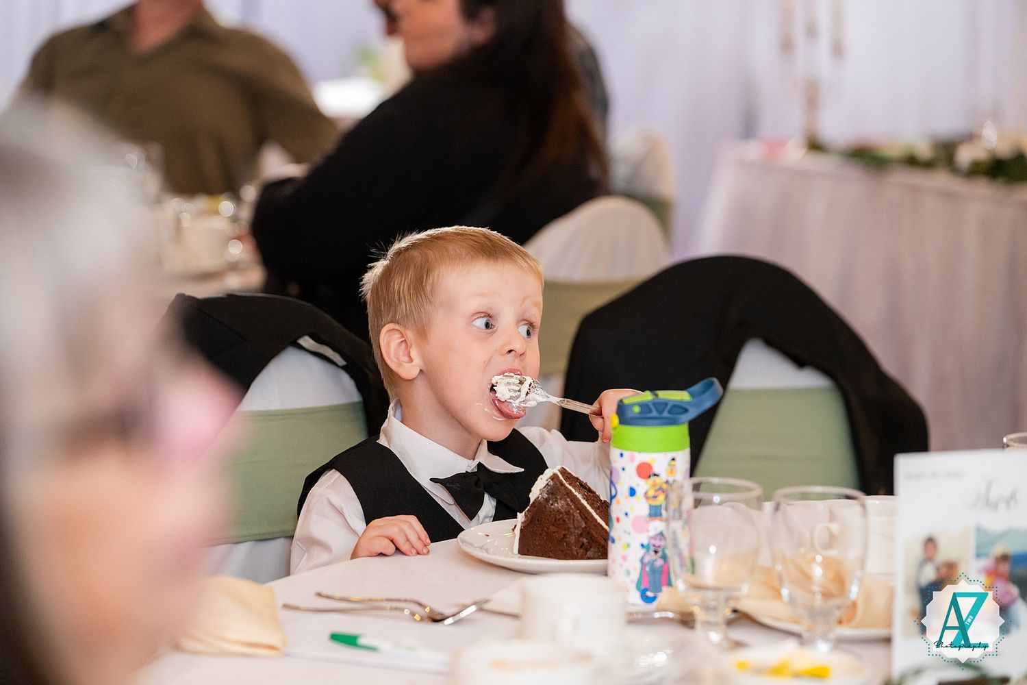 A small child sits at a dining table looking upward while holding a beverage cup.