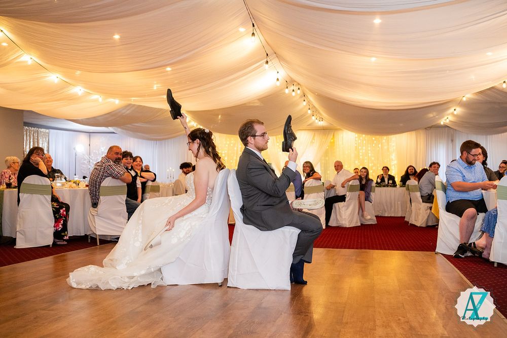 Wedding reception guests participate in a fun party game on the dance floor under draped fabric and string lights.