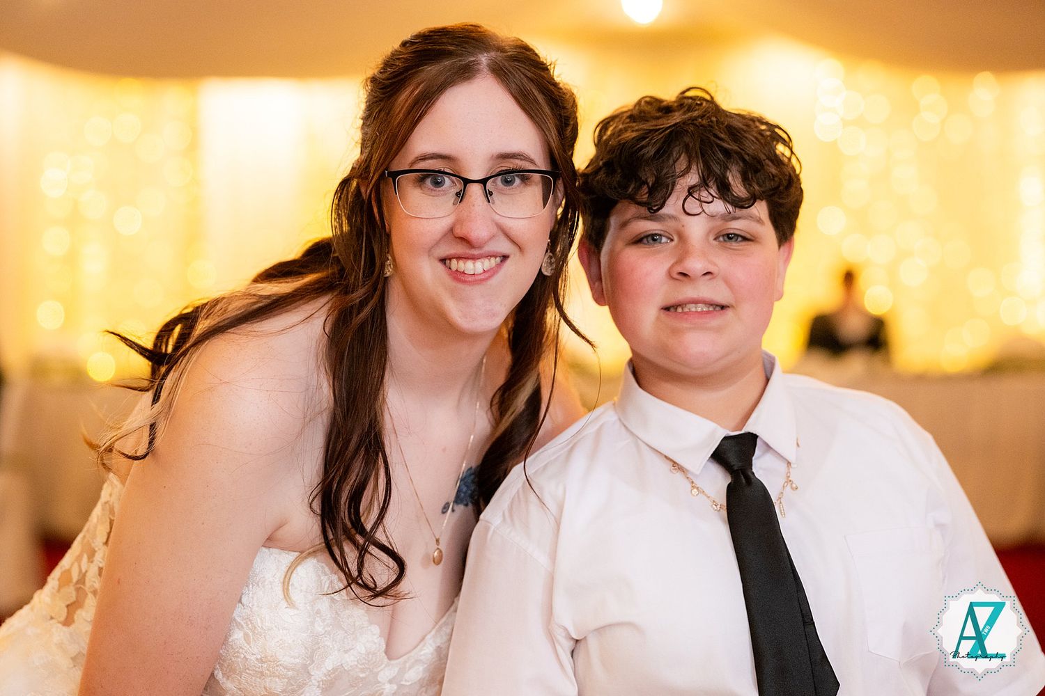 A happy couple poses together at their wedding reception with warm lighting in the background.