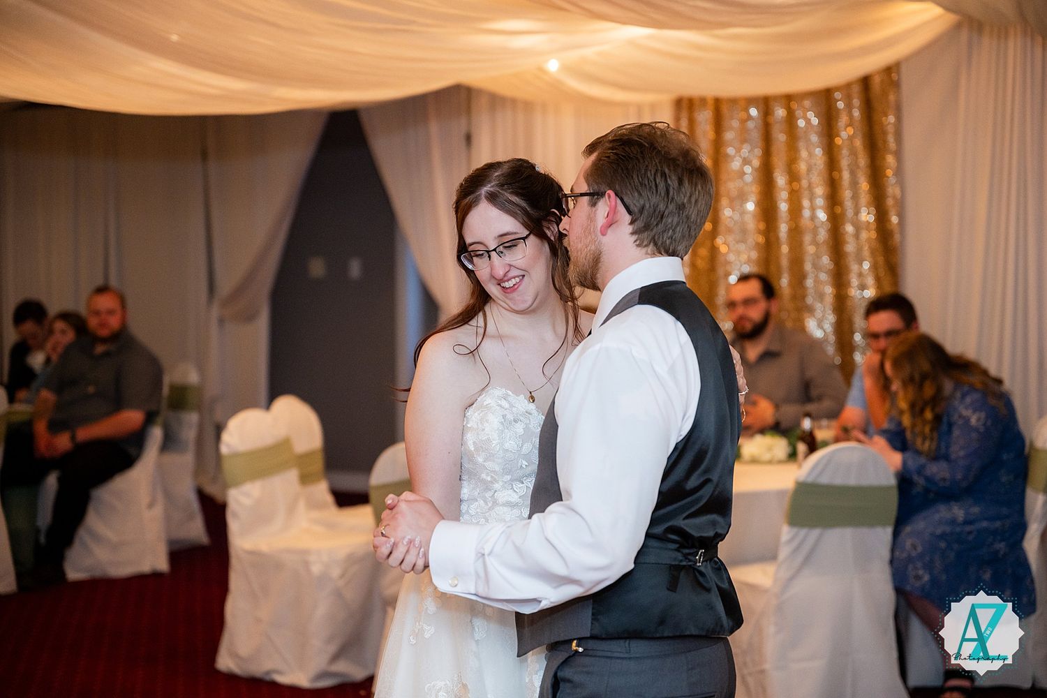 A couple dances together in an elegant reception hall decorated with flowing fabric drapes and twinkle lights.