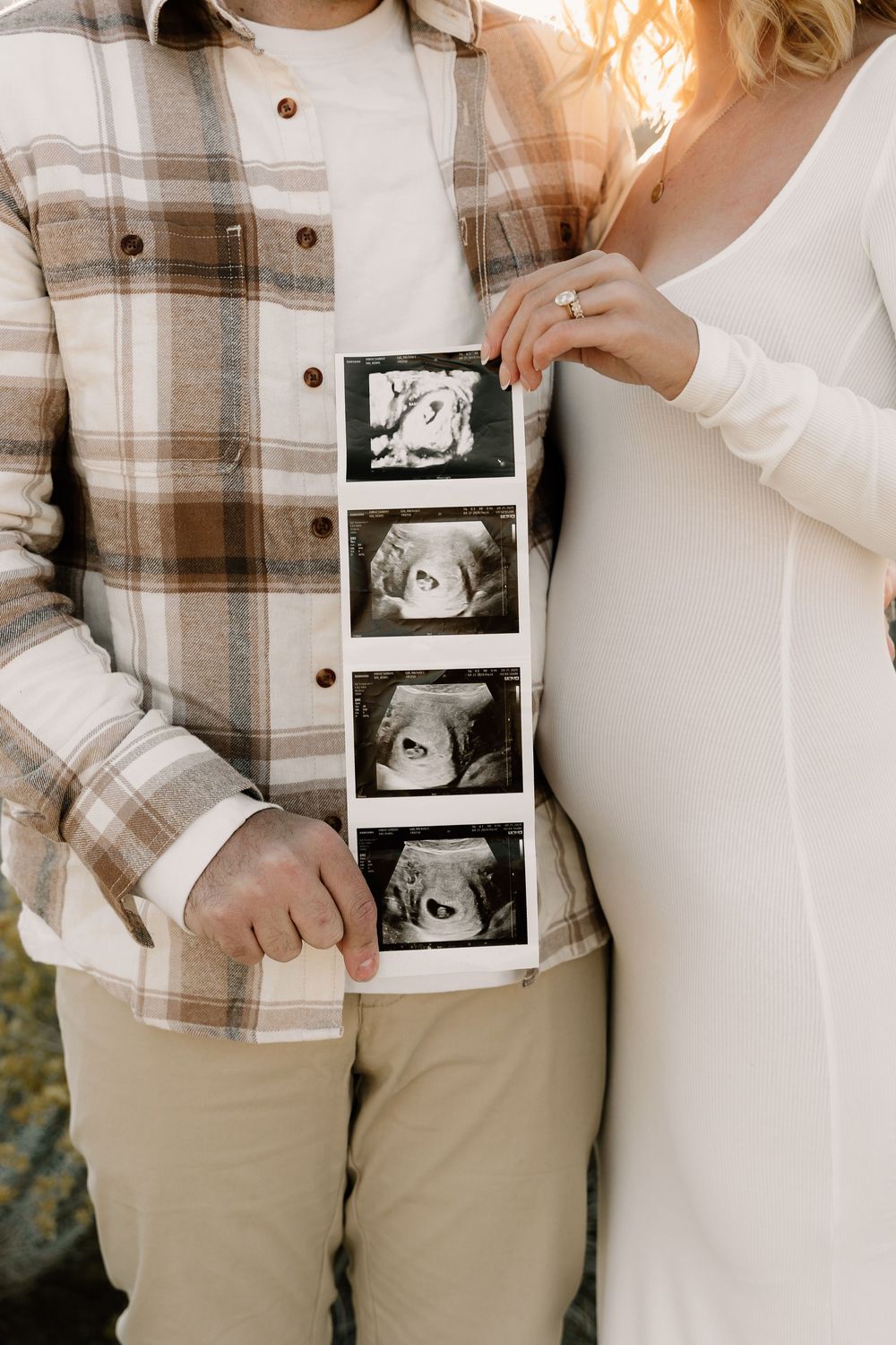 A couple in casual attire holds up ultrasound photos in a sweet pregnancy announcement moment.