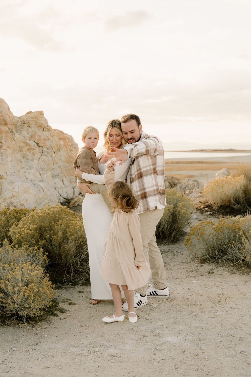 Family wearing coordinated neutral outfits poses together on rocky desert path at sunset.