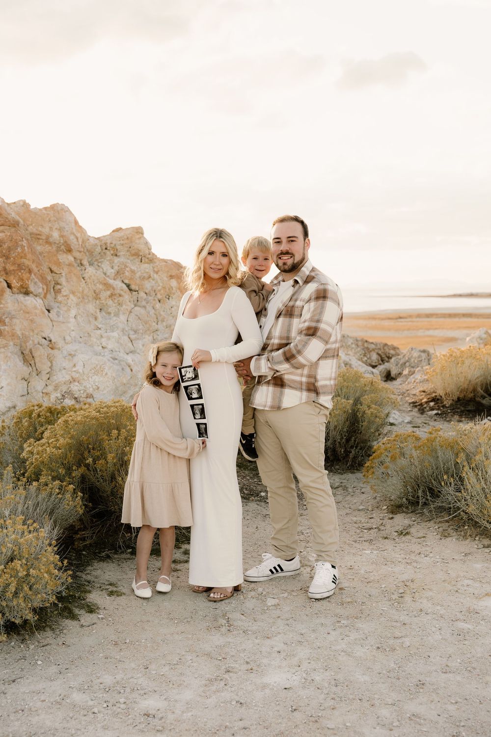 Family stands together on rocky cliff overlooking desert landscape at sunset, holding 2024 sign.