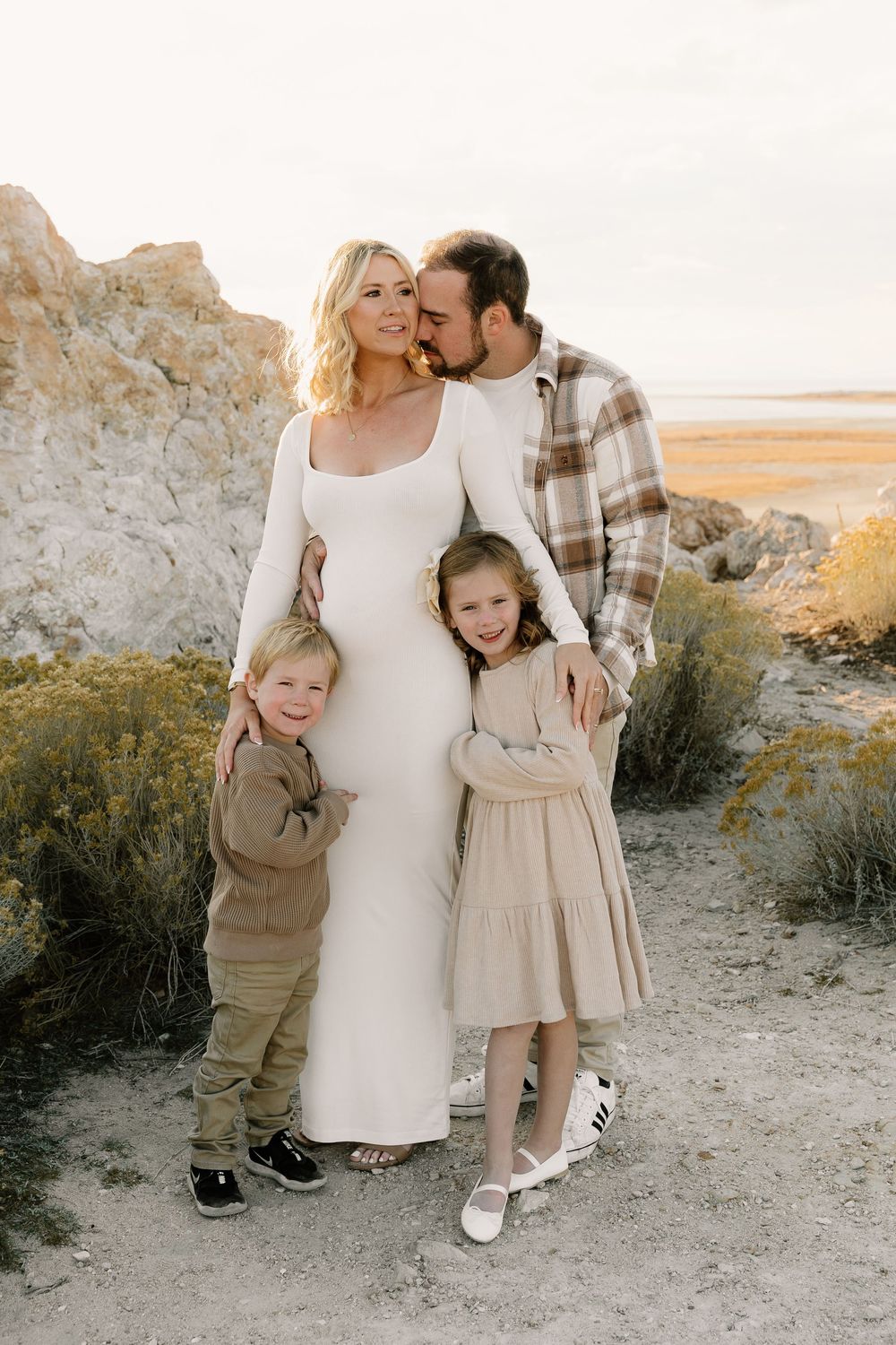 Family of four poses together at sunset on a rocky outdoor trail wearing coordinating neutral-toned outfits.
