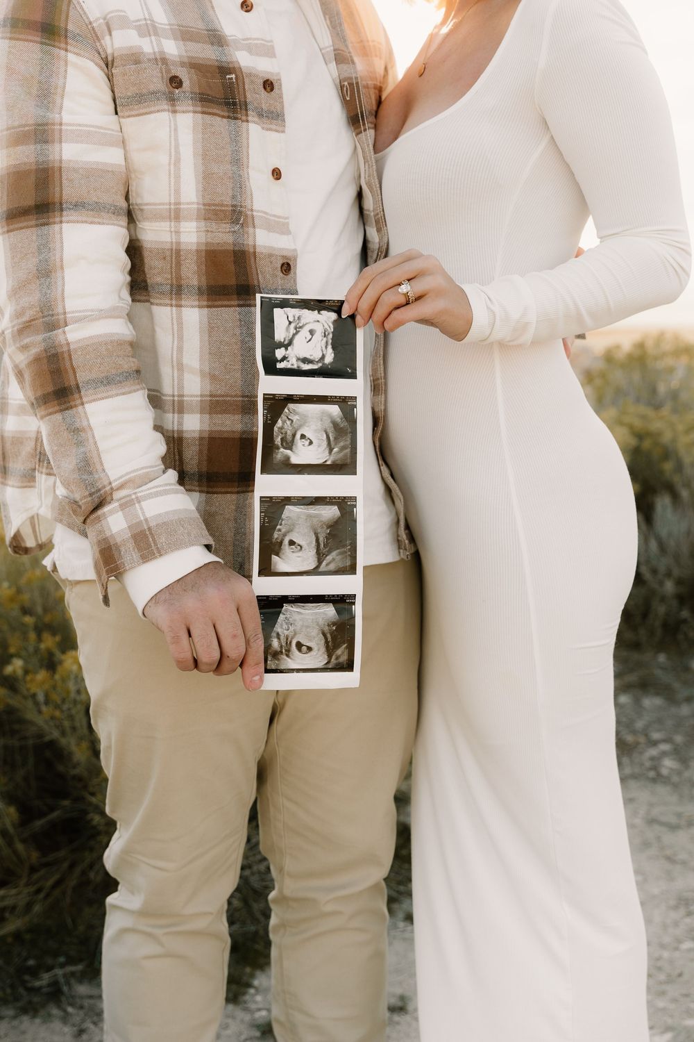 A couple holds ultrasound photos while wearing coordinating neutral outfits during their pregnancy announcement photoshoot.