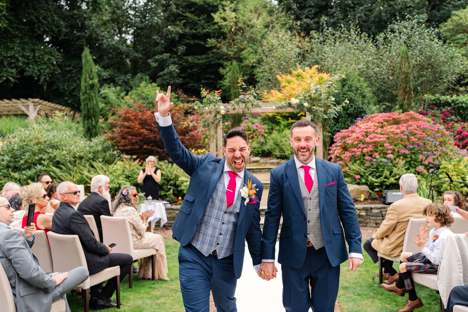 Two newlyweds celebrate while walking down the aisle in a garden ceremony surrounded by wedding guests.