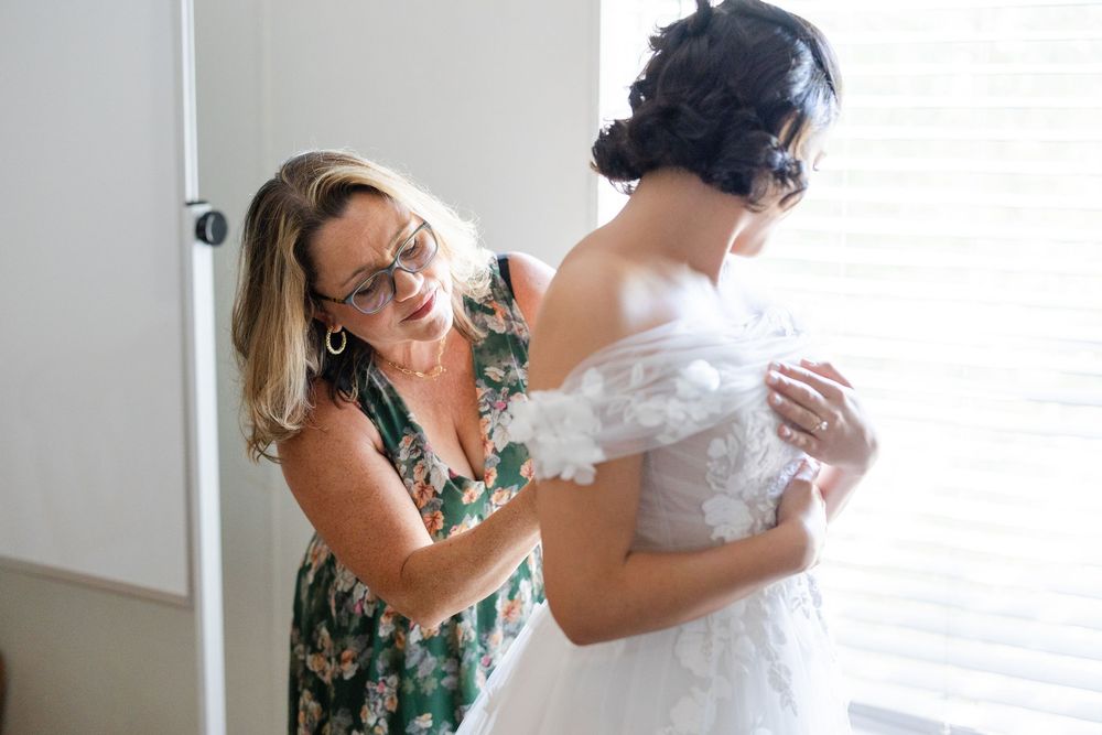 A touching moment as someone helps adjust a wedding dress during preparation.