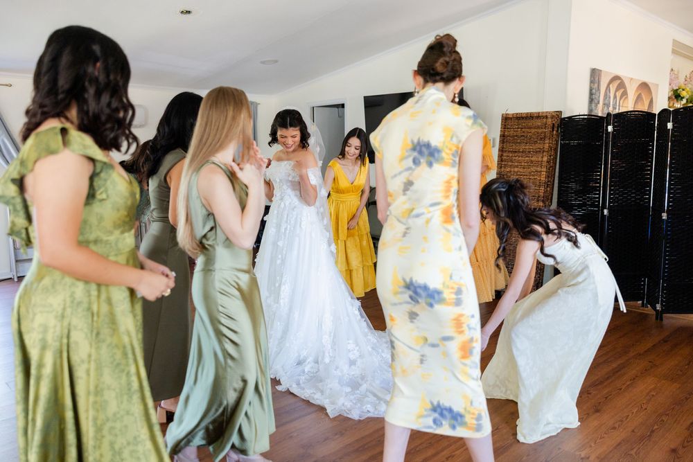 Bridesmaids in pastel dresses laugh and dance together during a wedding celebration.