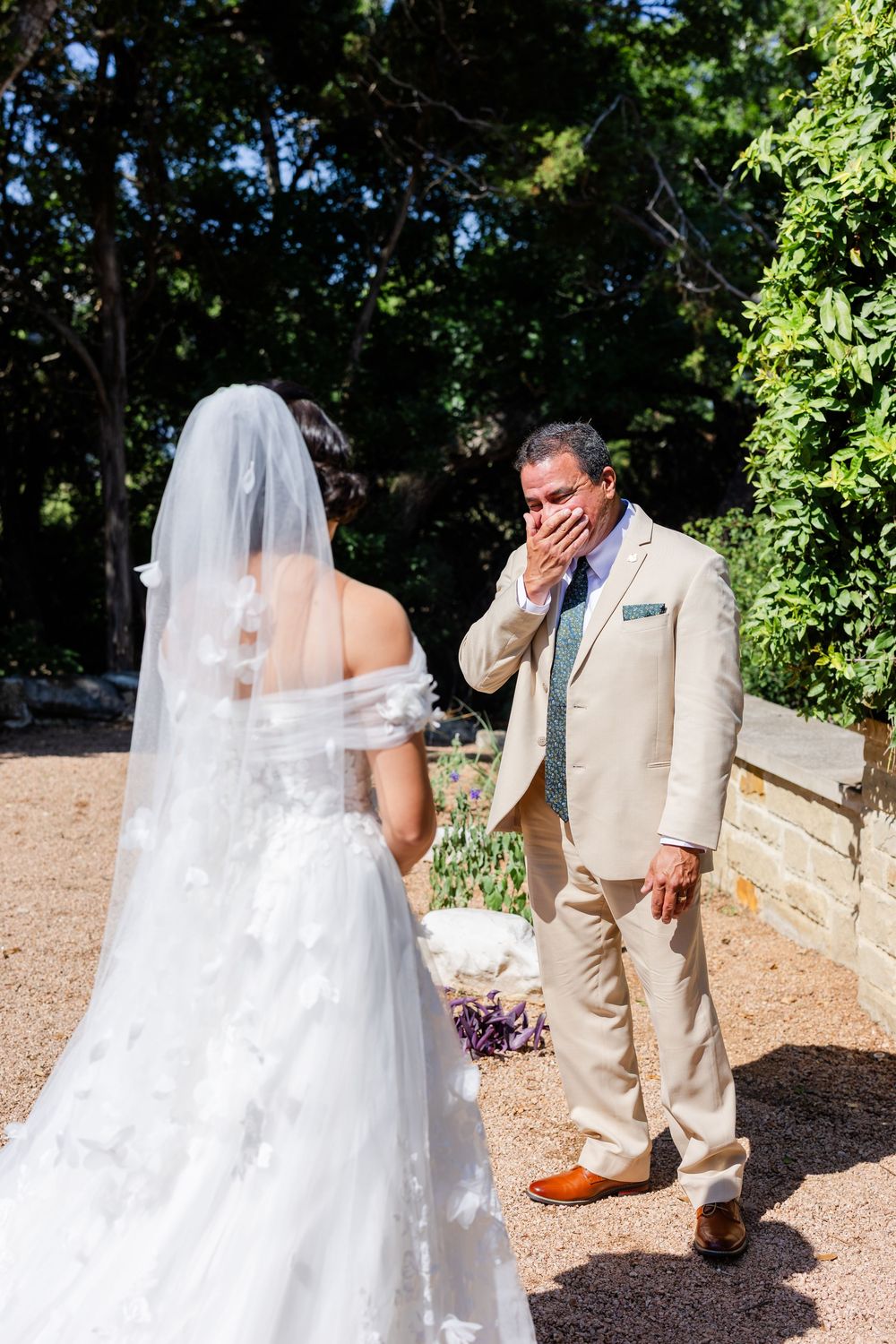 An emotional first look moment at an outdoor wedding with the bride in a white gown and groom in a beige suit.