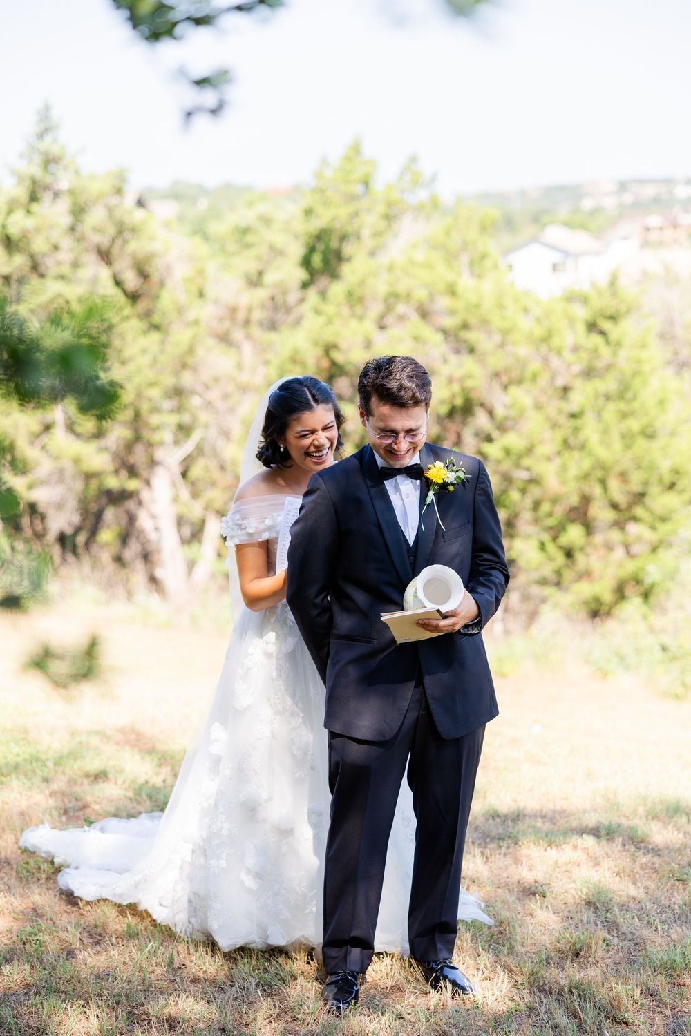 A joyful wedding couple share a candid moment together on a sunny hillside.