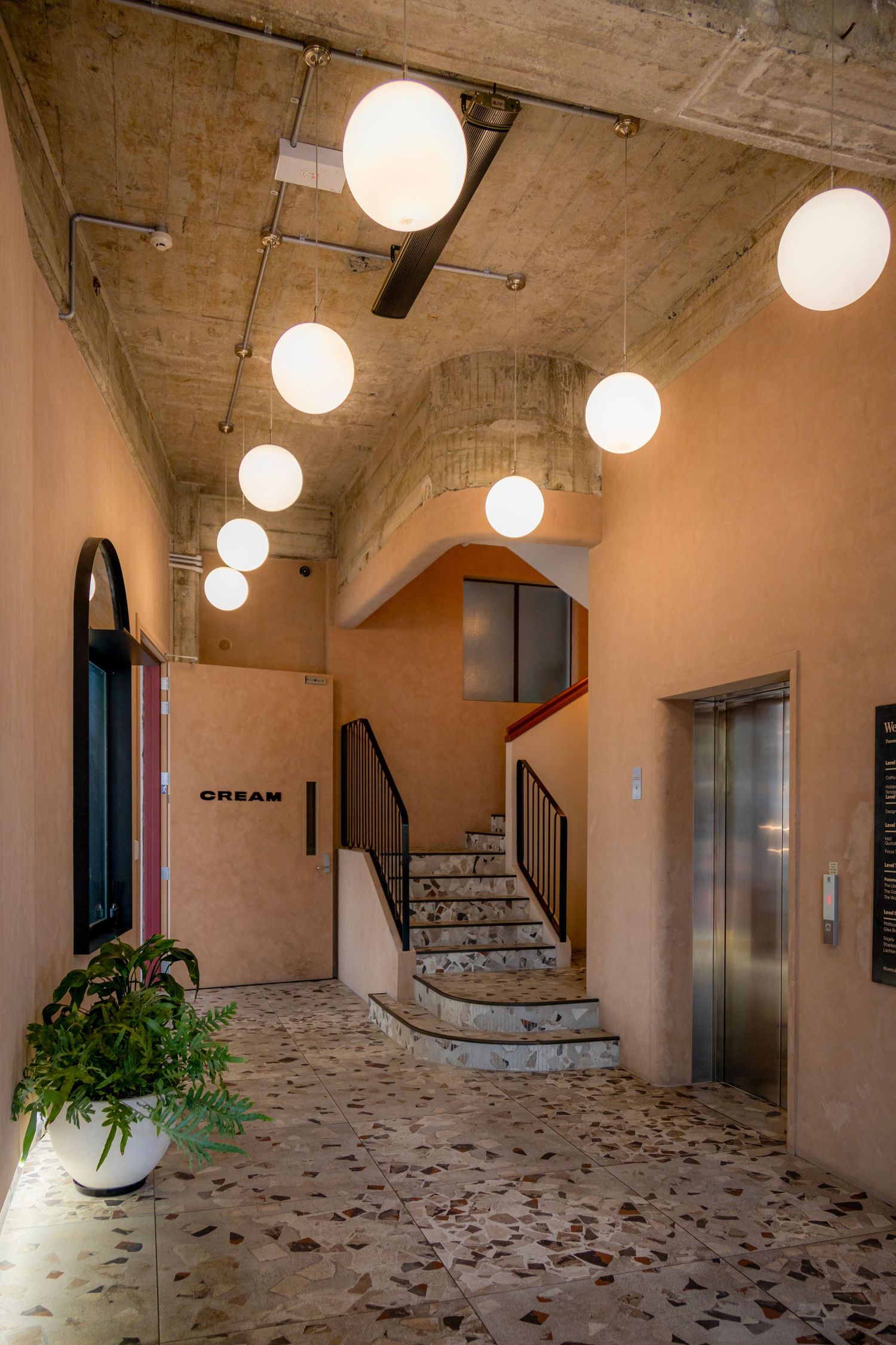 Warm-toned hallway with globe pendant lights, terrazzo flooring, and stair access to cinema rooms.