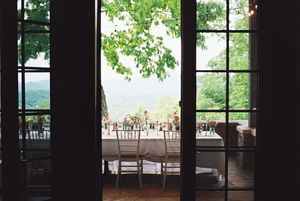 View through French doors of an elegant outdoor restaurant terrace with dining tables overlooking a scenic landscape.
