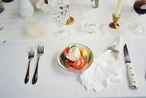 Table setting at wedding reception with caprese salad appetizer, white linens, and elegant place settings.