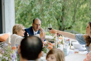 People enjoying drinks and conversation at an elegant outdoor table setting with flowers and glassware.