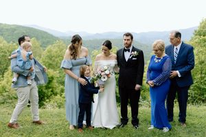 Wedding party stands together outdoors on a hilltop with green mountains and trees in the background.