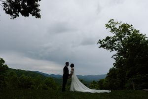 Silhouettes of a couple stand against a misty mountain backdrop with dramatic stormy skies overhead.