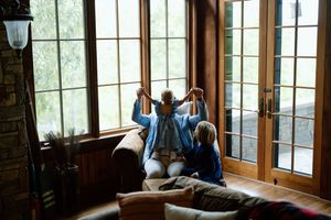 Three people sit together on a window bench in a rustic room with large windows and natural light.