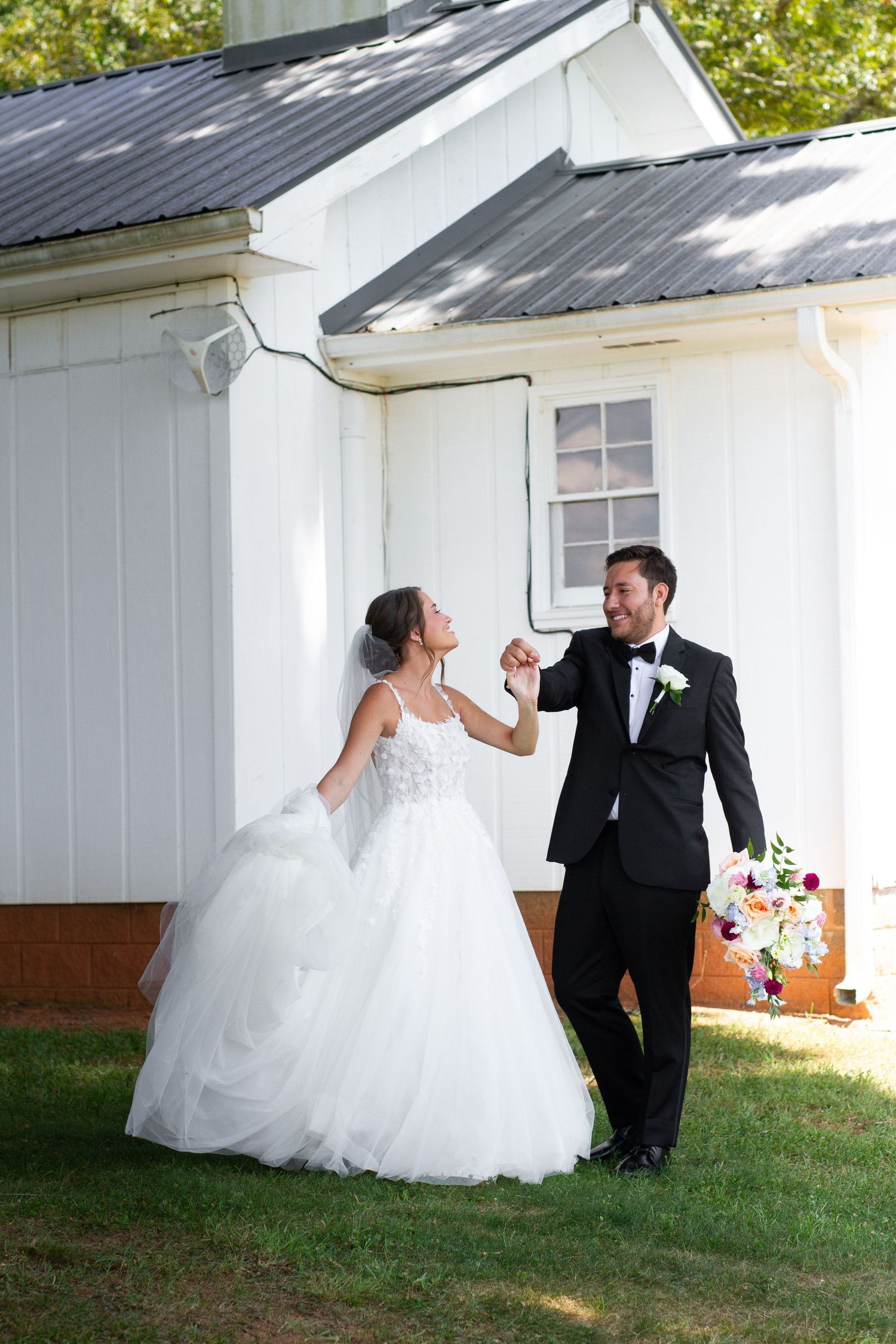 Playful wedding couple poses against white barn wall in sequence of romantic shots.